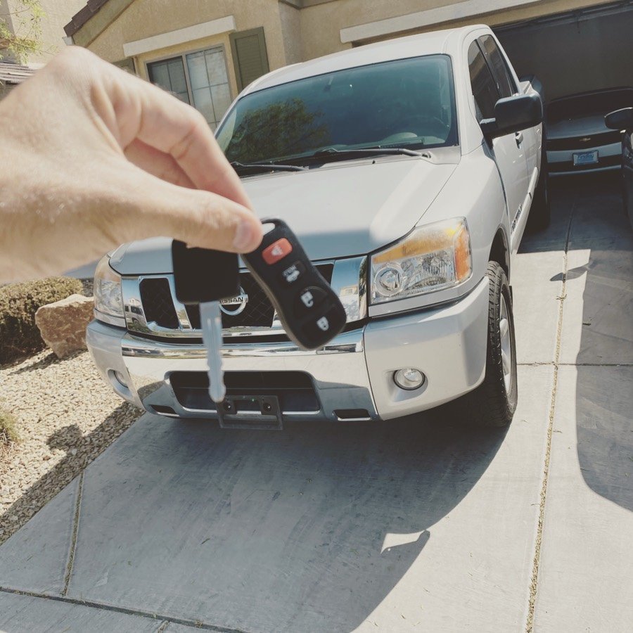 Replacement Nissan key and remote held in front of a Nissan Titan in Las Vegas